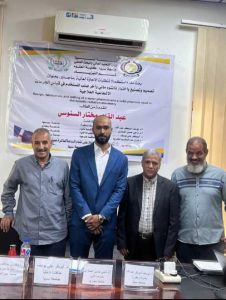 FE042BA4-23B7-4A1A-A13B-8E062A367C4A - جامعة سبها | Sebha University Four men pose for a photo at a conference in front of a banner about water treatment design and testing in Arabic text on the wall poster.