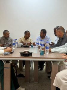 WhatsApp Image 2026-07-12 at 11.32.21 PM - جامعة سبها | Sebha University Group of men seated around a wooden conference table in discussion, with bottled water, cups, and papers on the table.