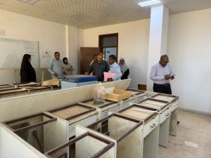 WhatsApp Image 2026-07-12 at 11.32.22 PM (2) - جامعة سبها | Sebha University Group of people in a classroom or workshop, examining old lab benches and a blue device on the counter.