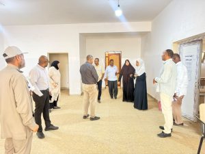 WhatsApp Image 2026-07-12 at 11.32.25 PM (1) - جامعة سبها | Sebha University A diverse group of ten adults standing in a circle in a bright hallway, conversing during a meeting or tour.