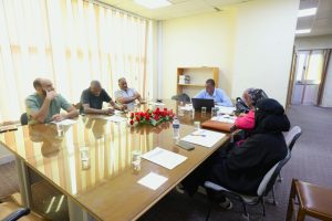 4916015B-62E0-4757-9F09-BE1979BD59CA - جامعة سبها | Sebha University Six adults seated around a glass conference table in a bright office, some taking notes and a laptop open nearby.