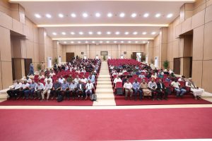 C06357D8-FFCB-41E2-AC00-76C7C2561049 - جامعة سبها | Sebha University Audience seated in a modern auditorium with red chairs during a conference or event.
