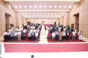 Large conference hall filled with people standing in a red-seat auditorium, posing for a group photo.