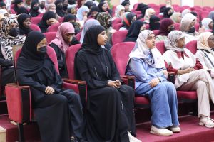 D4996818-9BC5-4EB3-855A-5915CABF3101 - جامعة سبها | Sebha University Group of women wearing hijabs seated in red theater seats, some wearing face masks, attending an event in a large auditorium.
