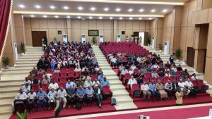 EB51EADA-D580-4D05-82D7-43F79130A776 - جامعة سبها | Sebha University Audience seated in red chairs in a large auditorium facing the stage.