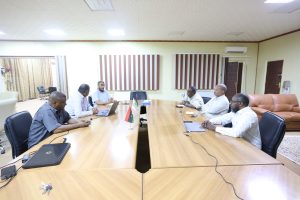 inbound1367757688805021472 - جامعة سبها | Sebha University Six men sit around a long wooden conference table in a meeting room, with laptops and small flags at the center of the table.