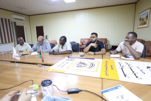 inbound602419541105348093 - جامعة سبها | Sebha University Group of men seated around a conference table in a meeting room, papers and a large poster spread out on the table in front of them.