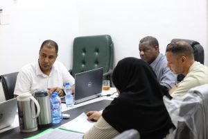 0DC0AE40-B13D-4F44-8DBB-06D0377A3BA0 - جامعة سبها | Sebha University Five professionals in a meeting around a conference table with a Dell laptop and beverages present on the table.