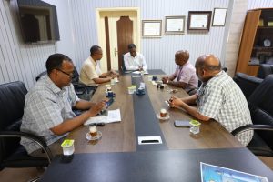 23F8EC26-1DD6-4E5B-982C-7361845DC790 - جامعة سبها | Sebha University Six professionals sit around a long conference table in a formal meeting room, with papers and coffee cups in front of them.