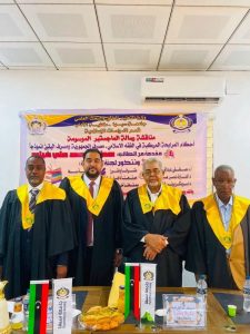 3FFDD077-9A38-4A1E-9368-D0586EF16760 - جامعة سبها | Sebha University Four men in academic gowns with yellow stoles stand in a row at a ceremony in front of an Arabic banner.