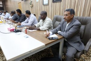 Group of men in a boardroom seated at a long table, taking notes during a meeting.
