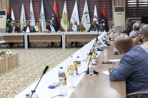 6B87B5DD-C3EC-428F-BB7D-3BDBA4273304 - جامعة سبها | Sebha University Formal meeting room with officials seated along a long conference table, flags behind them and microphones at each seat.