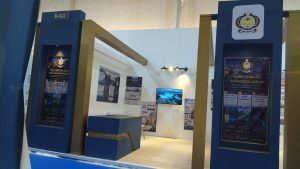 Exhibition booth with blue and gold pillars displaying posters in Arabic and a monitor on the wall behind.