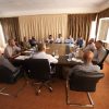 Approximately fourteen professionals seated around a rectangular conference table in a meeting room, engaged in discussion.