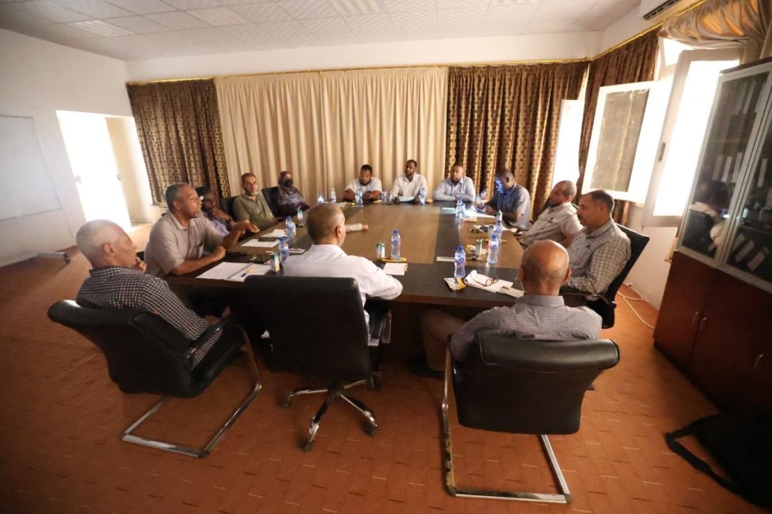 Approximately fourteen professionals seated around a rectangular conference table in a meeting room, engaged in discussion.