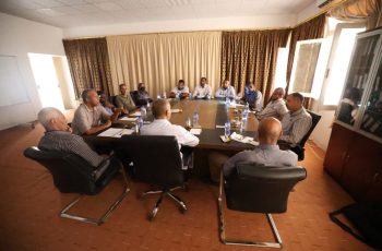 Approximately fourteen professionals seated around a rectangular conference table in a meeting room, engaged in discussion.