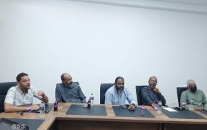 8489DBA7-F8F8-4F8F-9B14-BFFFF2D82E22 - جامعة سبها | Sebha University Five men sit along a long conference table in a meeting room, with water bottles and papers in front of them.