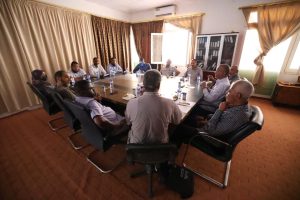 Group of professionals seated around a large rectangular conference table in a meeting room, engaged in discussion.