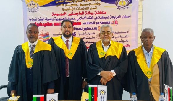 Four men in black academic robes with yellow hoods stand in front of a banner at a formal event, flags and snacks on the table in front of them.