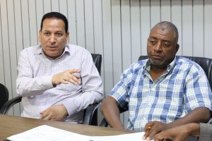 C5549E4F-3BF7-461B-AA06-1818DF062132 - جامعة سبها | Sebha University Two men seated at a conference table, one speaking and gesturing while the other listens in a meeting room.