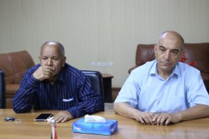 CD7BAD49-CCCD-4C0F-BD73-50E48C1374C8 - جامعة سبها | Sebha University Two men sit at a conference table in an office; one rests his chin on his hand while the other looks ahead.