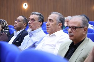 Group of middle-aged men in suits seated in a conference hall, listening attentively.