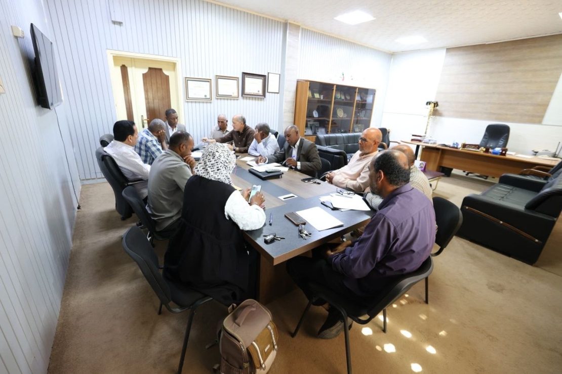 Group of professionals seated around a conference table in a meeting room, actively discussing documents and notes:**