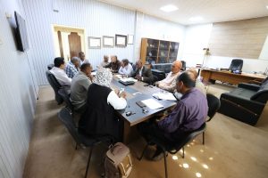 Group of professionals seated around a conference table in a meeting room, actively discussing documents and notes:**