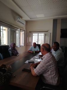 Five people sit around a long conference table in a bright office, engaged in a meeting with phones and papers on the table.