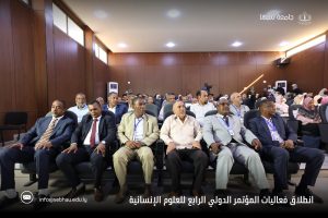 inbound1613755957209775847 - جامعة سبها | Sebha University Audience seated in a wood-paneled conference hall during a formal humanities conference, with Arabic title at the bottom and logos top-right.