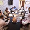 Group of men sitting around a conference table in a meeting room, discussing documents and notes.