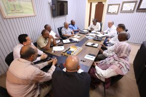 Group of men sitting around a conference table in a meeting room, discussing documents and notes.