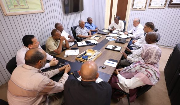 inbound2859835638980000573 - جامعة سبها | Sebha University Group of men sitting around a conference table in a meeting room, discussing documents and notes.