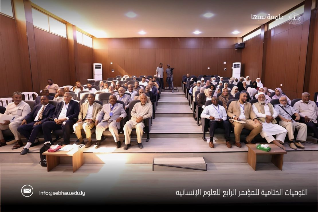 Audience seated in a university conference hall for the fourth humanitarian sciences conference, logo and Arabic title visible at top and bottom