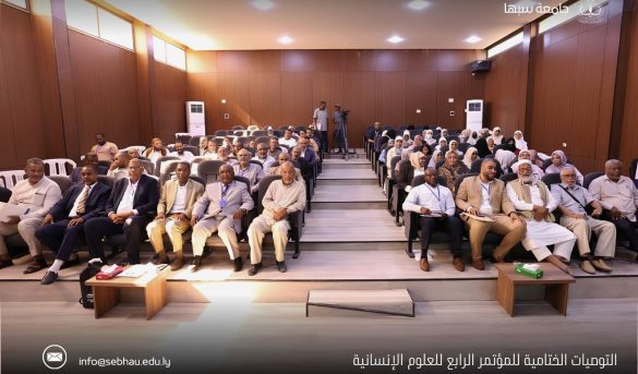 inbound3169740801652770798 - جامعة سبها | Sebha University Audience seated in a university conference hall for the fourth humanitarian sciences conference, logo and Arabic title visible at top and bottom