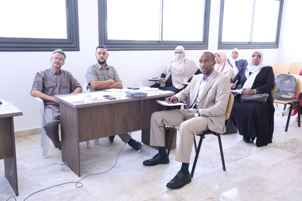 Group of professionals in a meeting room, seated at a wooden table with papers and water cups.