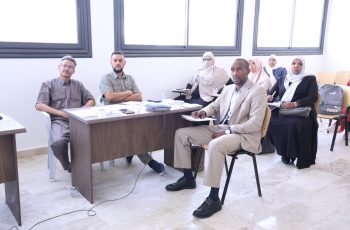 Group of professionals in a meeting room, seated at a wooden table with papers and water cups.