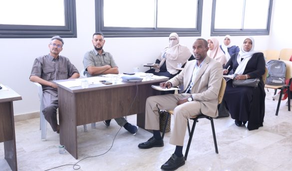 inbound3280351056625882162 - جامعة سبها | Sebha University Group of professionals in a meeting room, seated at a wooden table with papers and water cups.