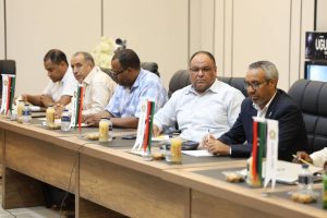 inbound3713730613681554944 - جامعة سبها | Sebha University Group of men in business attire seated at a long conference table with small national flags and drinks, in a formal meeting setting.