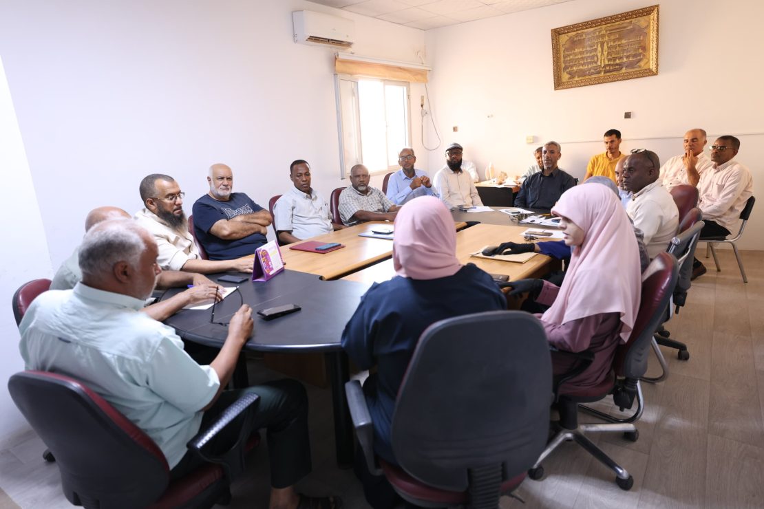Group of adults seated around a conference table in a meeting room, discussing and taking notes.