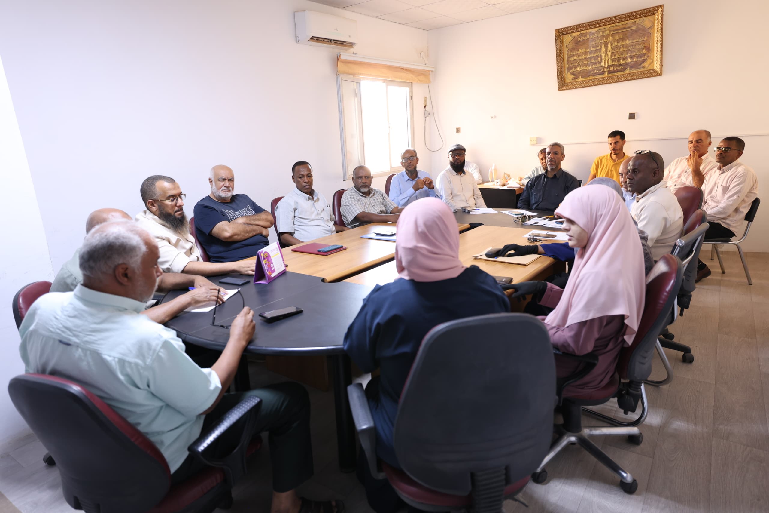 Group of adults seated around a conference table in a meeting room, discussing and taking notes.