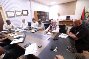 Group of professionals seated around a large conference table in a bright office, discussing documents and notes.