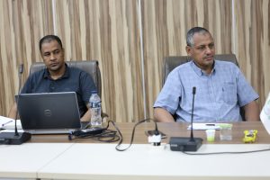 inbound4763531983706457840 - جامعة سبها | Sebha University Two men sit at a conference table with laptops and microphones during a meeting in a boardroom.