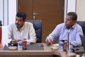 inbound5073585611664261854 - جامعة سبها | Sebha University Two men in a boardroom taking notes at a conference table with bottles and snacks nearby.