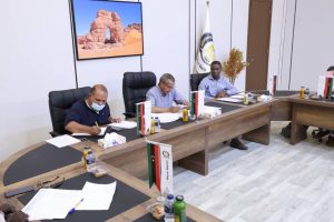 inbound6736163638087622203 - جامعة سبها | Sebha University Group of men in a conference room signing documents at a long table with Libyan flags nearby.