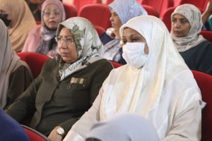 Group of women wearing hijabs seated in a red auditorium, attending a meeting or seminar.