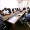 Group of men in business casual sit around a long conference table in a meeting room on a workday (informative scene).