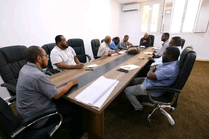 1792536219992 - جامعة سبها | Sebha University Group of men in business casual sit around a long conference table in a meeting room on a workday (informative scene).