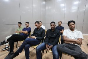 4U1A0544 - جامعة سبها | Sebha University Group of young men seated in chairs along a wall in a modern room, some looking at phones or ahead.