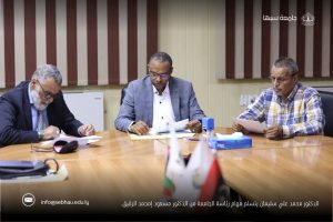 FB_IMG_1791396839691 - جامعة سبها | Sebha University Three men in business attire sit at a conference table reviewing documents, with flags visible in the foreground and an Arabic caption across the bottom.